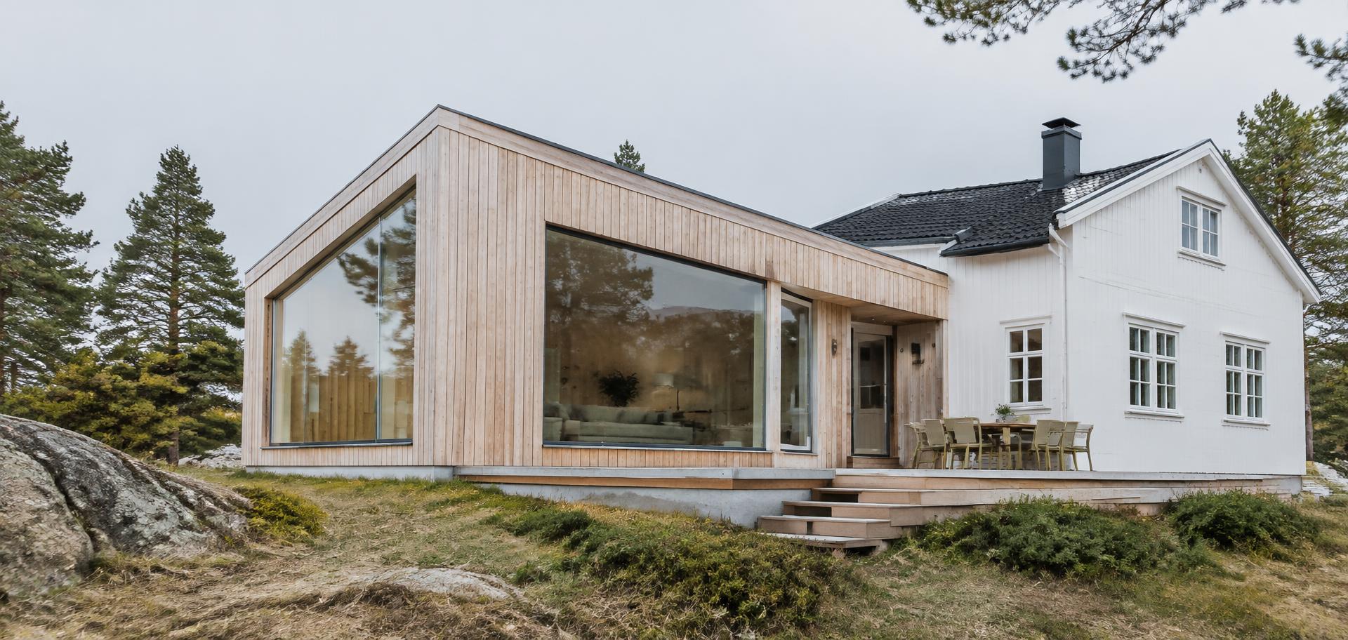 Moderne tilbygg i lys trekledning på et tradisjonelt hvitt trehus